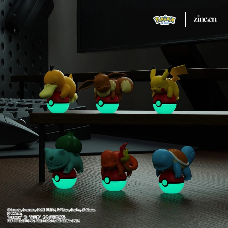 Glowing toy figures of Pokémon characters on a desk with a computer monitor in the background.