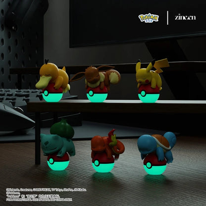 Glowing toy figures of Pokémon characters on a desk with a computer monitor in the background.